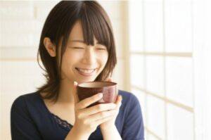 味噌汁を笑顔で飲む女性
